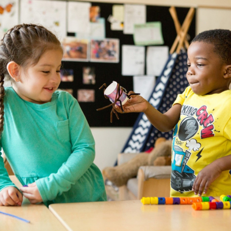 Preschool girl and boy A preschool student shows his classmate a spider he made from pipe cleaners and a paper cup.
